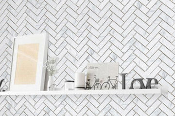 Matte carrara herringbone mosaic porcelain floor and wall tile featured on wall with white floating shelf holding various decor items